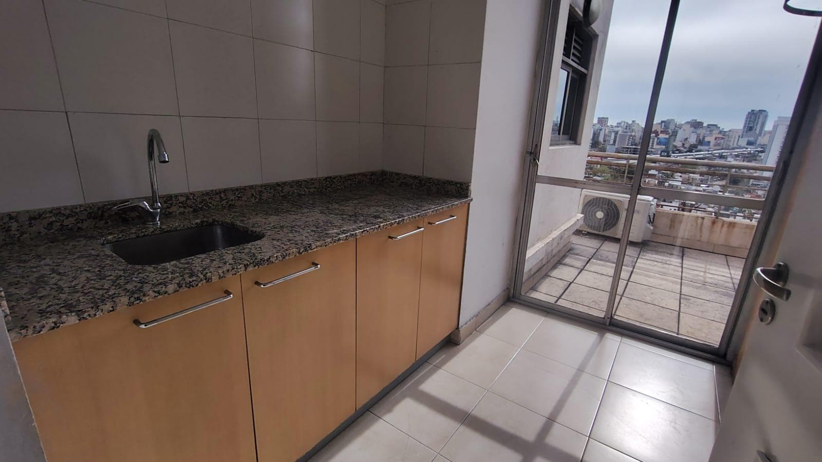 Mesada con bacha y alacenas, salida a balcón, vista exterior.