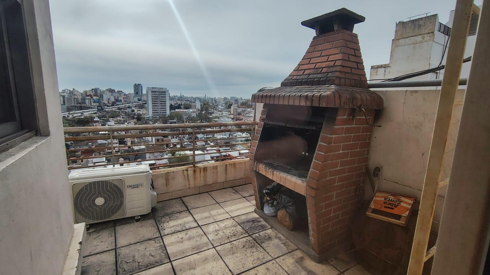 Parrilla exterior de ladrillo en terraza común, vista a la ciudad.