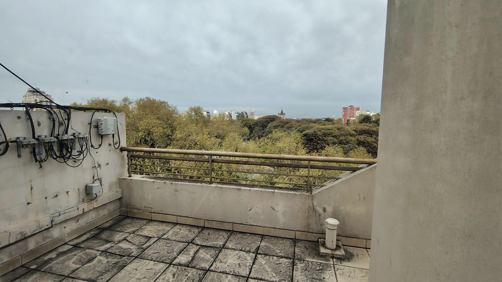 Terraza común del edificio con vista a árboles y ciudad.