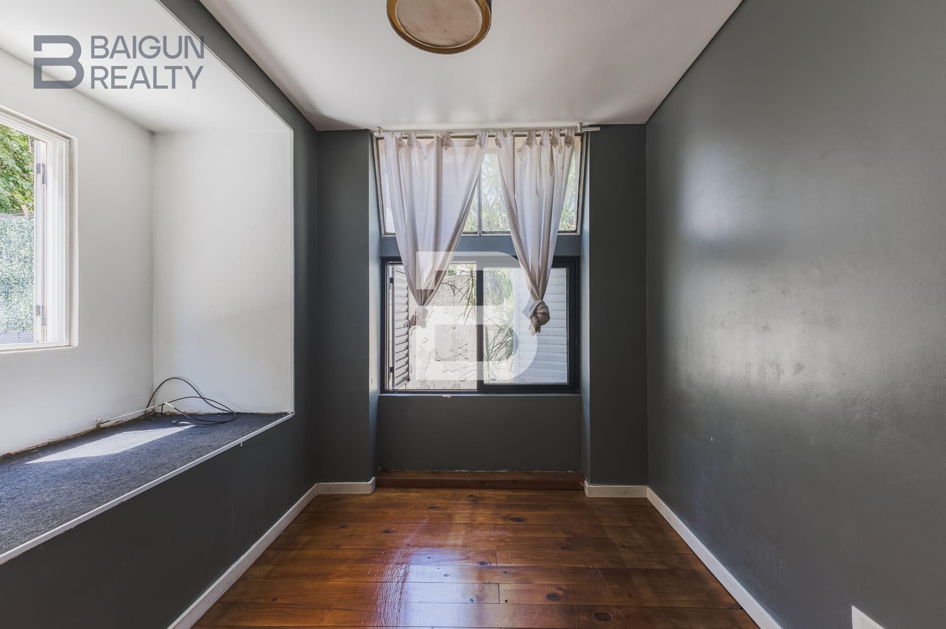 Dormitorio vacío con ventanas y paredes grises.