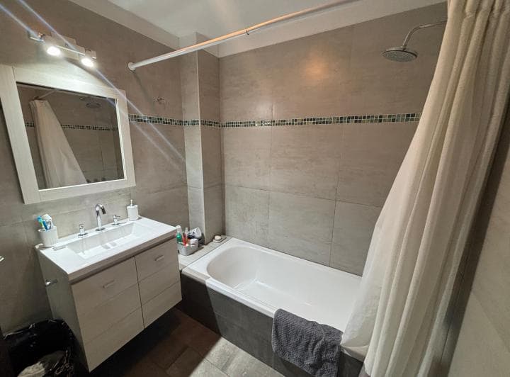 Baño con bañera, ducha, vanitory con espejo y azulejos grises.