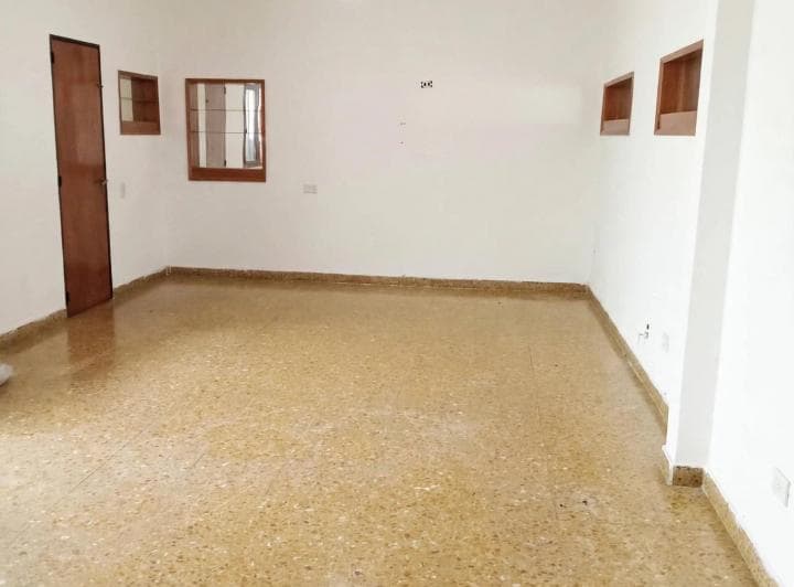 Habitación vacía con piso de granito, puerta de madera y ventanas pequeñas.