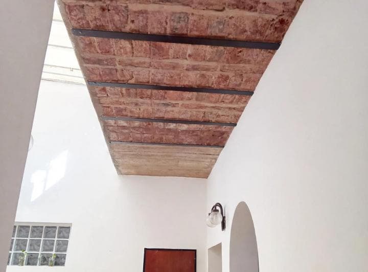 Pasillo con techo de ladrillo visto, pared blanca, luz y un arco.