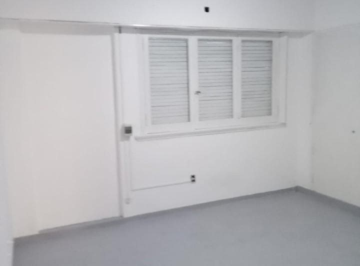 Cuarto vacío con ventana grande de celosía, paredes blancas y piso gris.