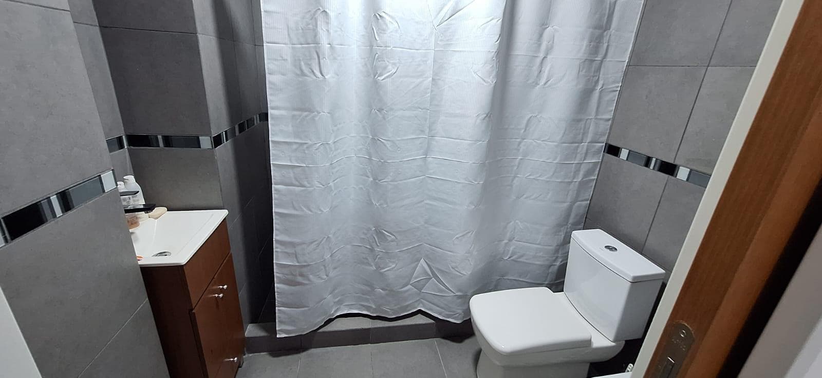 Baño completo con inodoro, lavatorio y cortina de ducha gris.