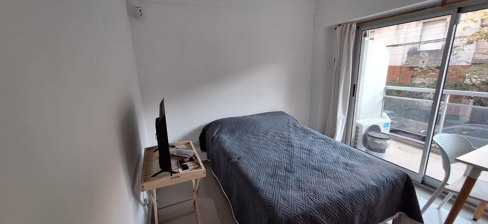 Dormitorio con cama individual, televisión y acceso al balcón.