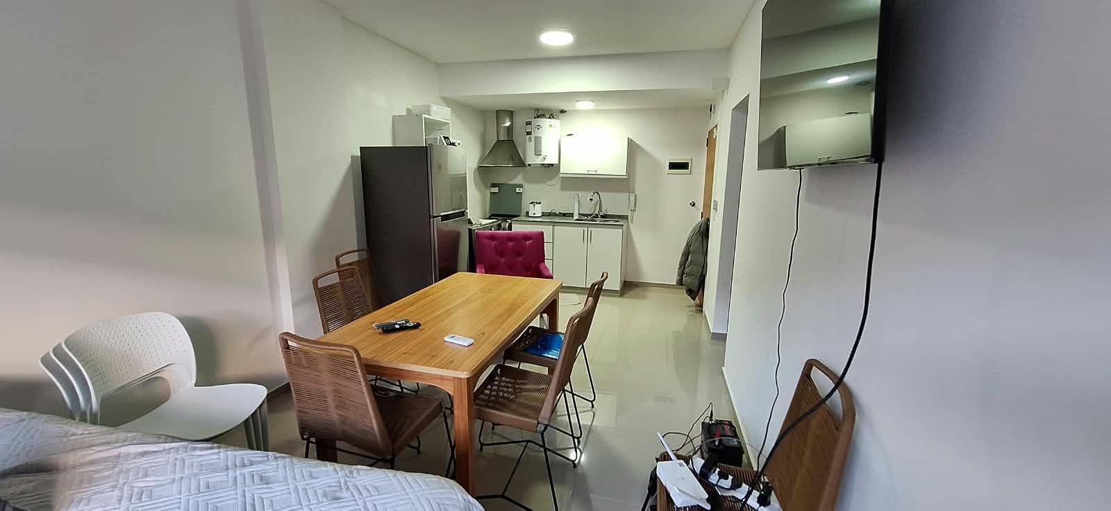 Living-comedor con mesa de madera, sillas y cocina integrada.