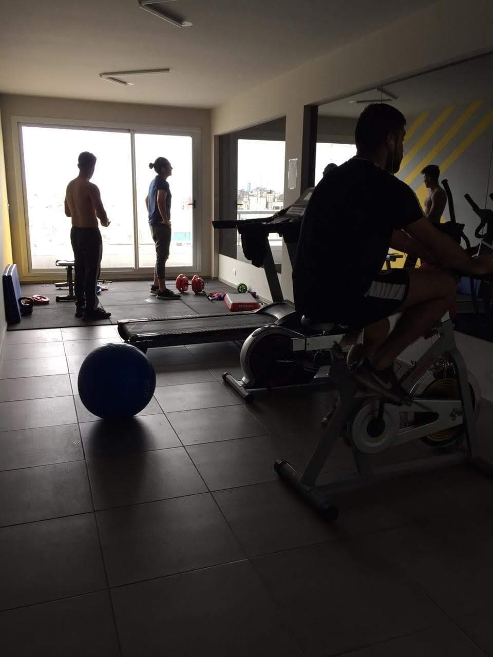 Gimnasio del edificio con máquinas de ejercicio y ventanales grandes.