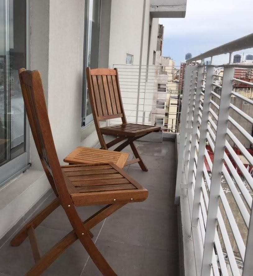 Balcón con dos sillas de madera y vistas a los edificios de la ciudad.