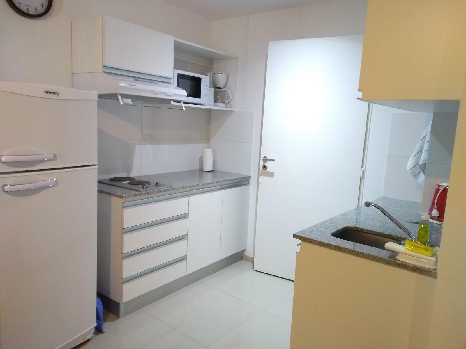 Cocina con heladera, anafe eléctrico y alacenas blancas.