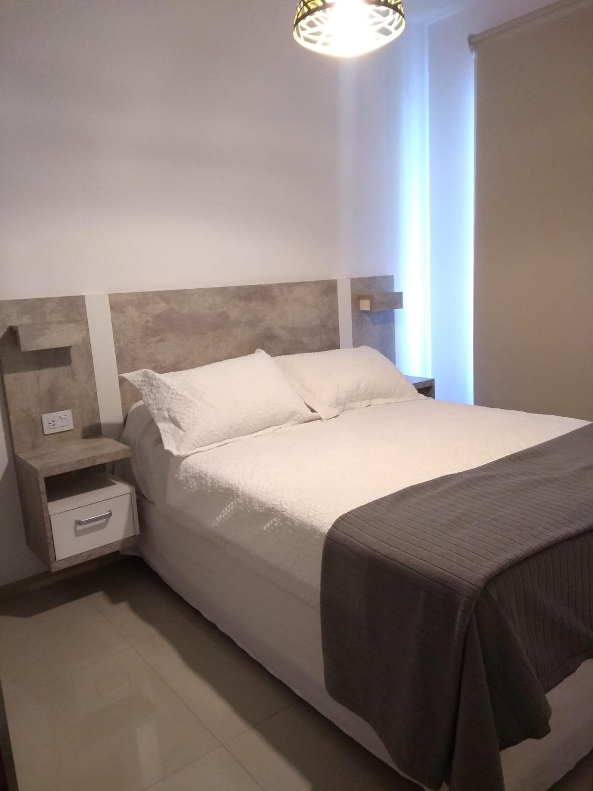 Dormitorio con cama de dos plazas, respaldo moderno y cortina roller.