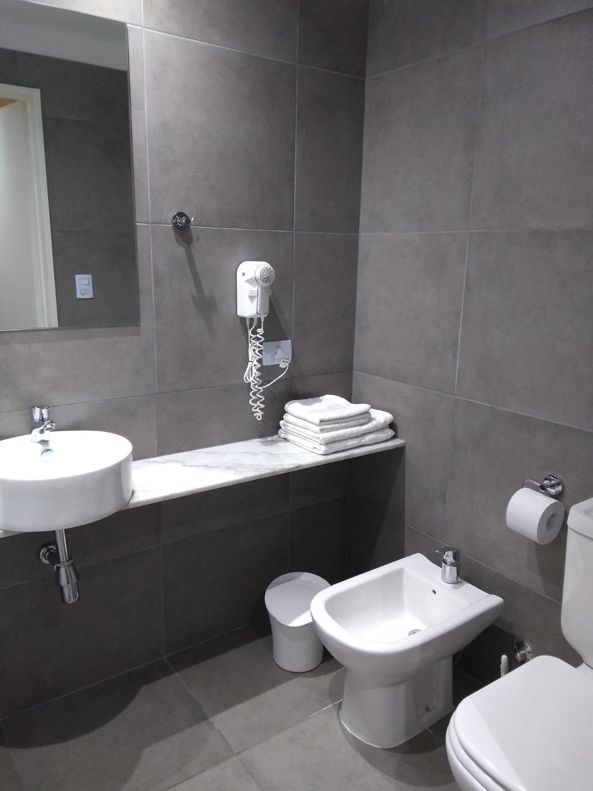 Baño moderno con bidet, inodoro, lavatorio y espejo grande.