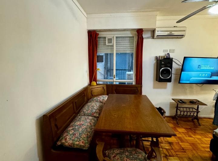 Living comedor con mesa de madera, banco esquinero, ventana y aire acondicionado.
