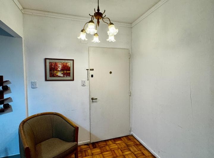 Hall de entrada con puerta blanca, una silla y un cuadro decorativo.