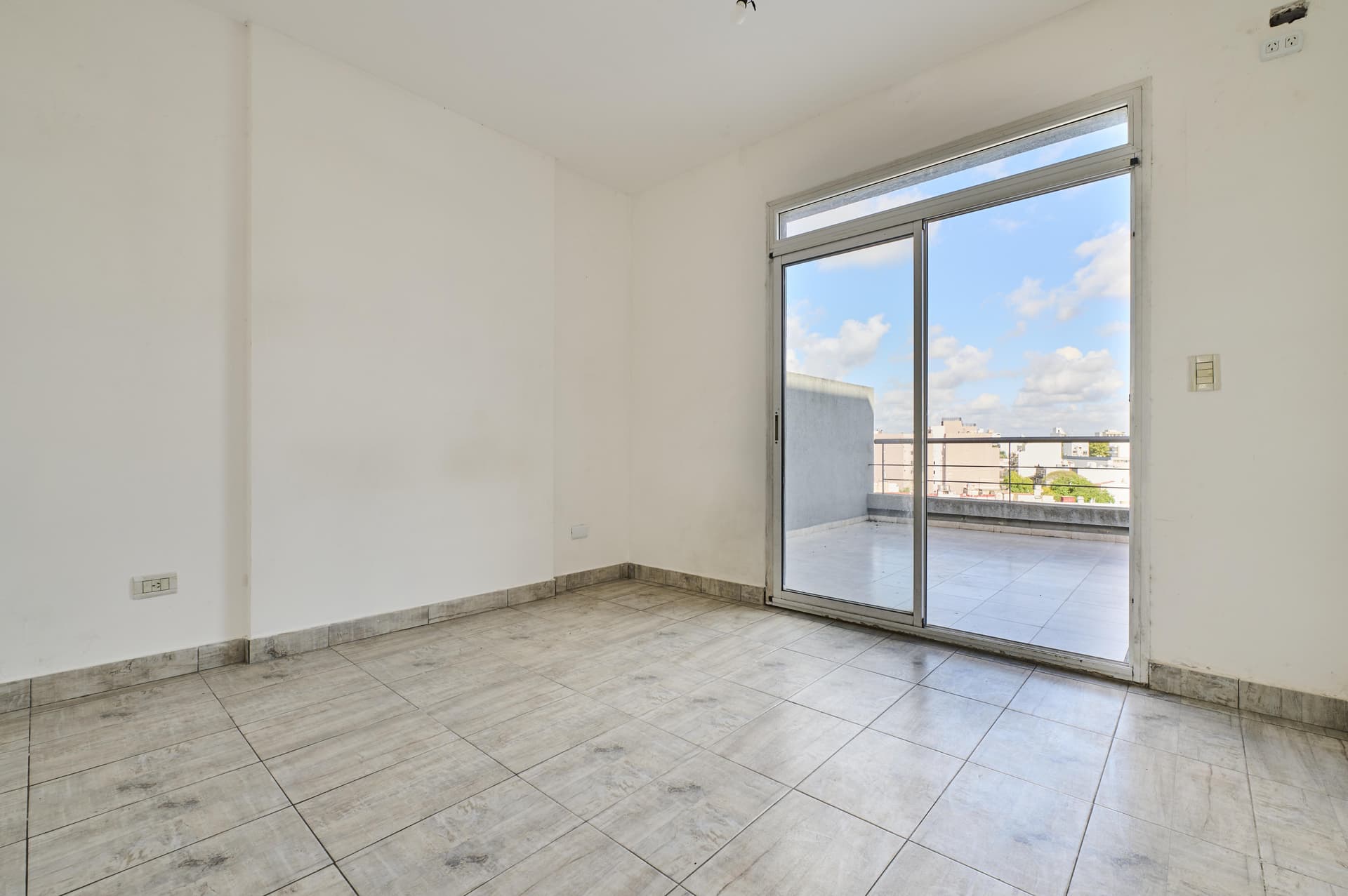 Dormitorio vacío con ventanal corredizo y acceso a la terraza privada.
