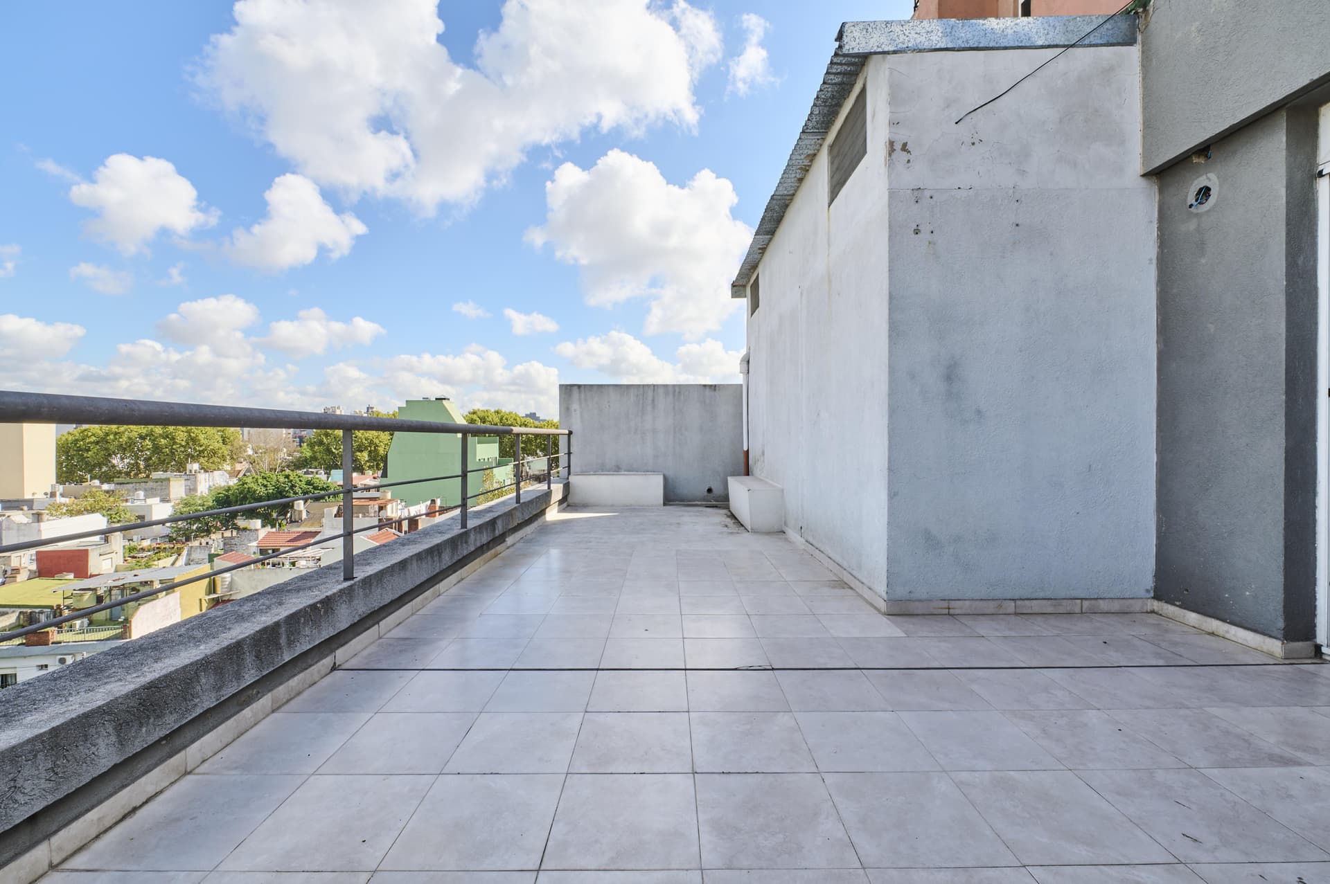 Amplia terraza en la azotea con baranda de metal y vistas a la ciudad.