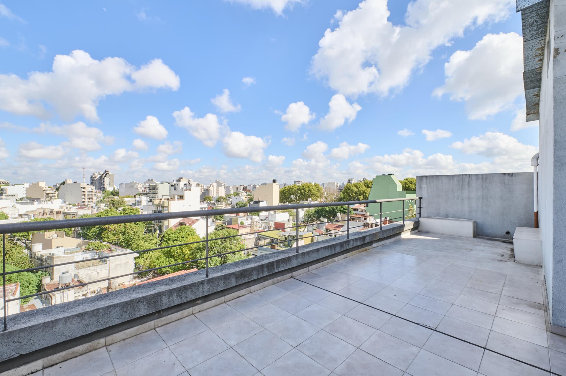 Terraza privada amplia con vistas panorámicas de la ciudad y cielo azul.