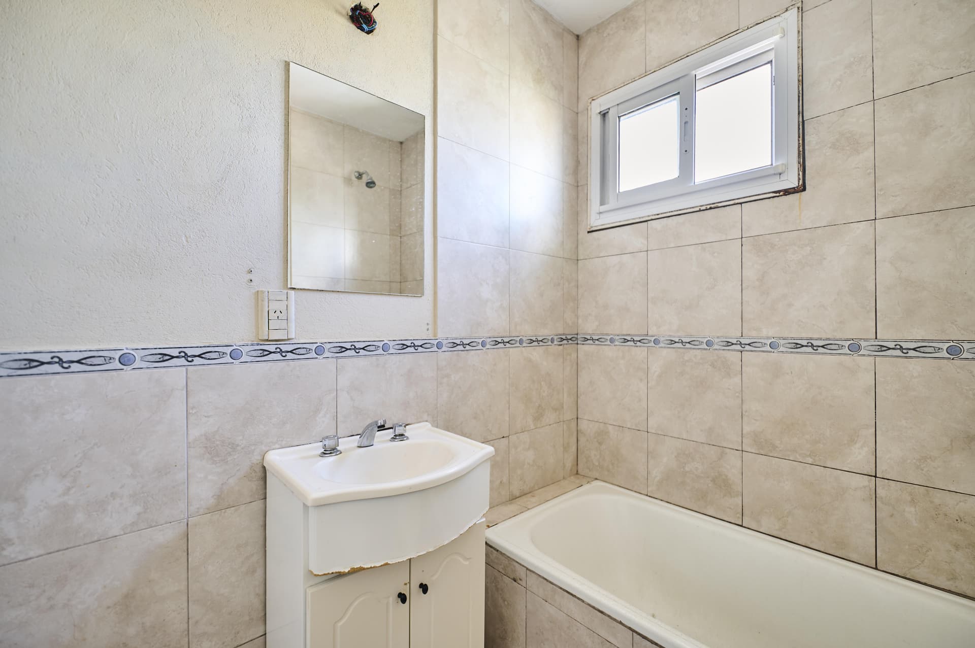 Baño con bañera, lavabo con vanitory, espejo y ventana, azulejos claros.