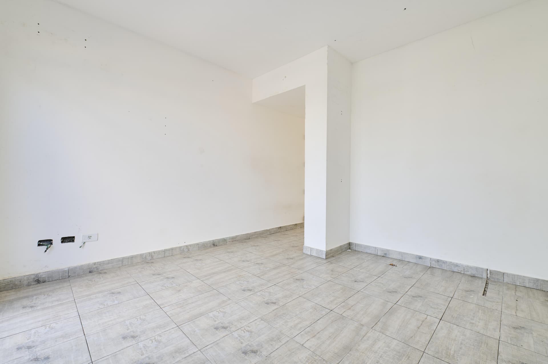 Cuarto vacío con piso cerámico y paredes blancas, posible área de paso.
