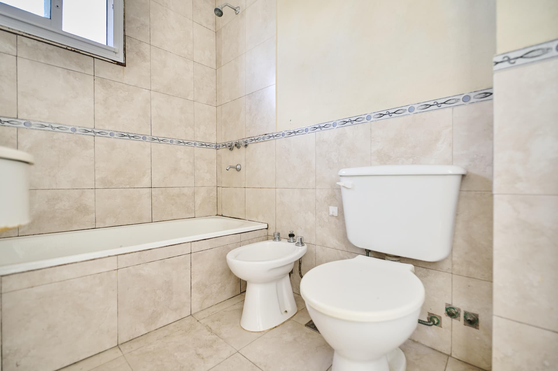 Baño con bañera, inodoro, bidet, ducha y azulejos decorados.