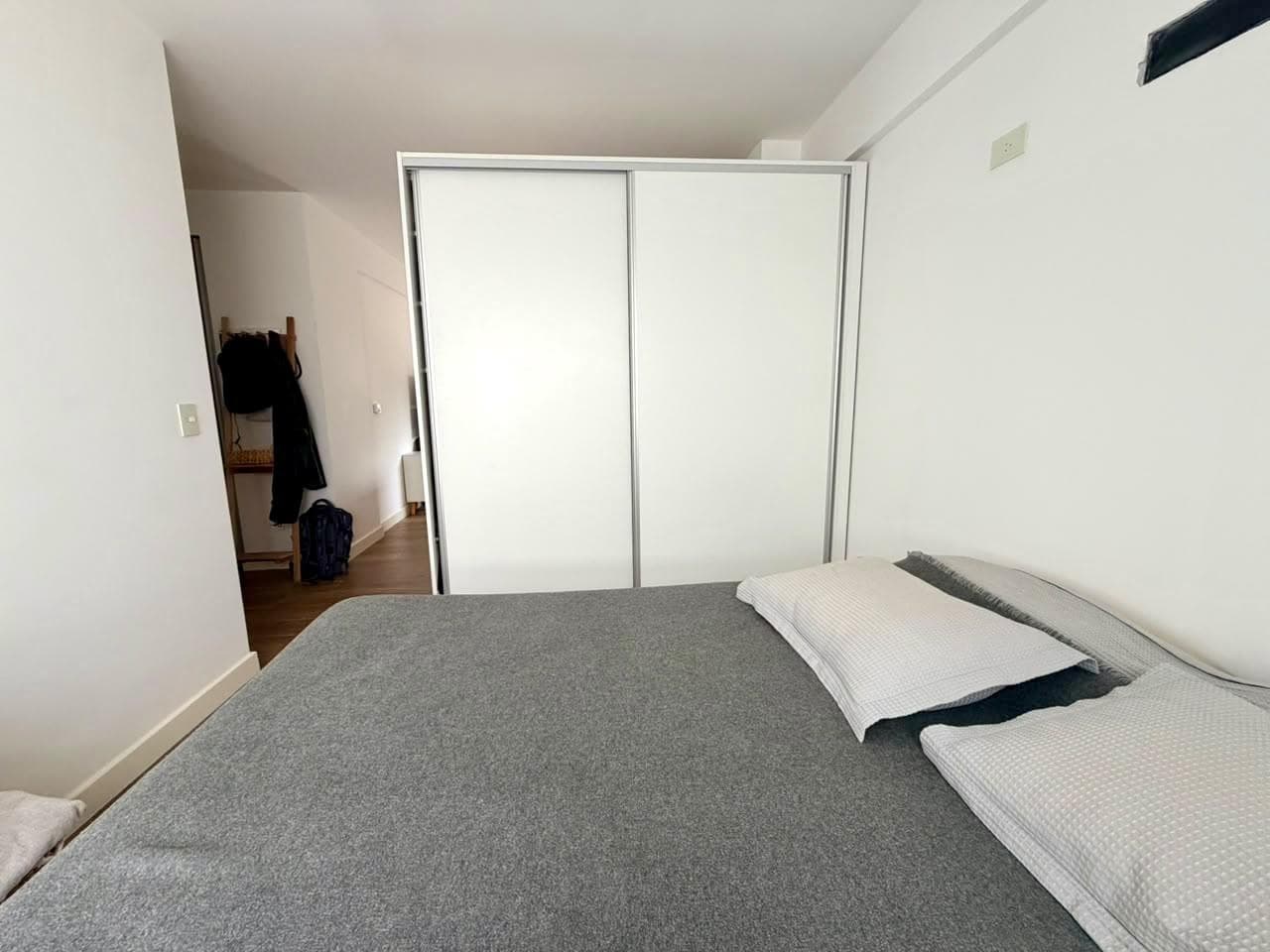 Dormitorio con cama doble y placard blanco, vista hacia la entrada.