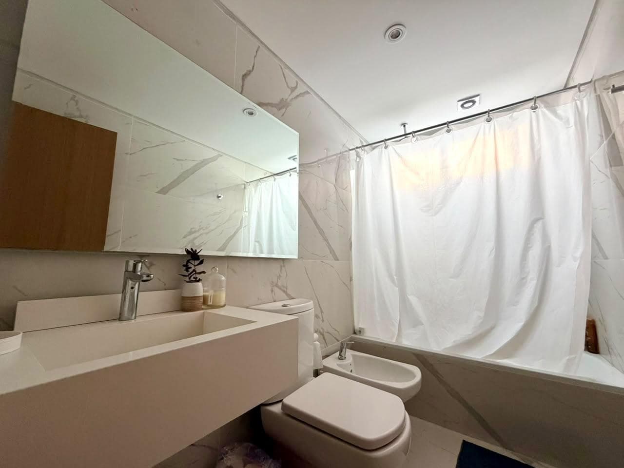 Baño completo con bañera, cortina de ducha, inodoro, bidet y lavatorio.