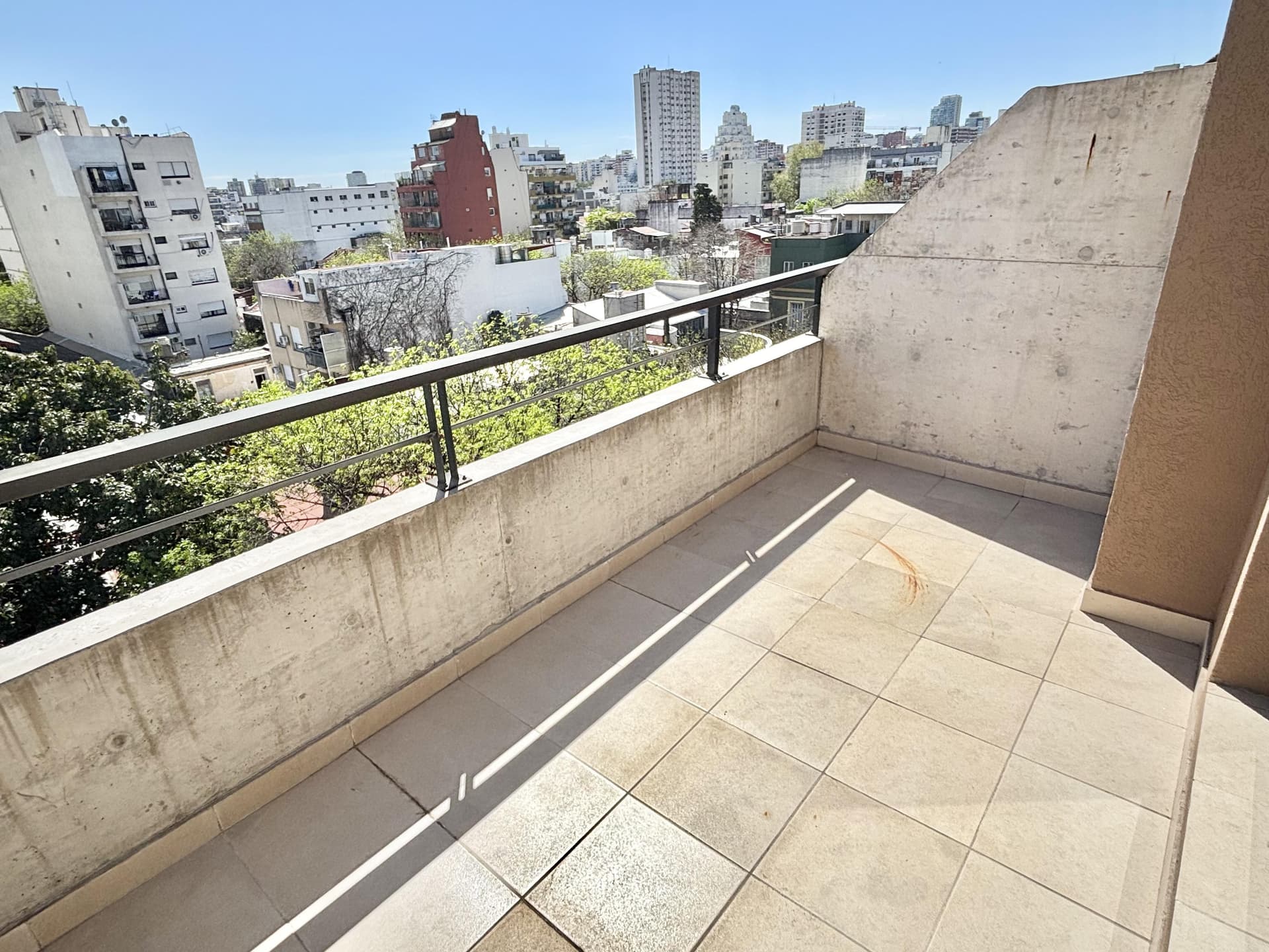 Balcón terraza amplio con baranda de cemento y metal.