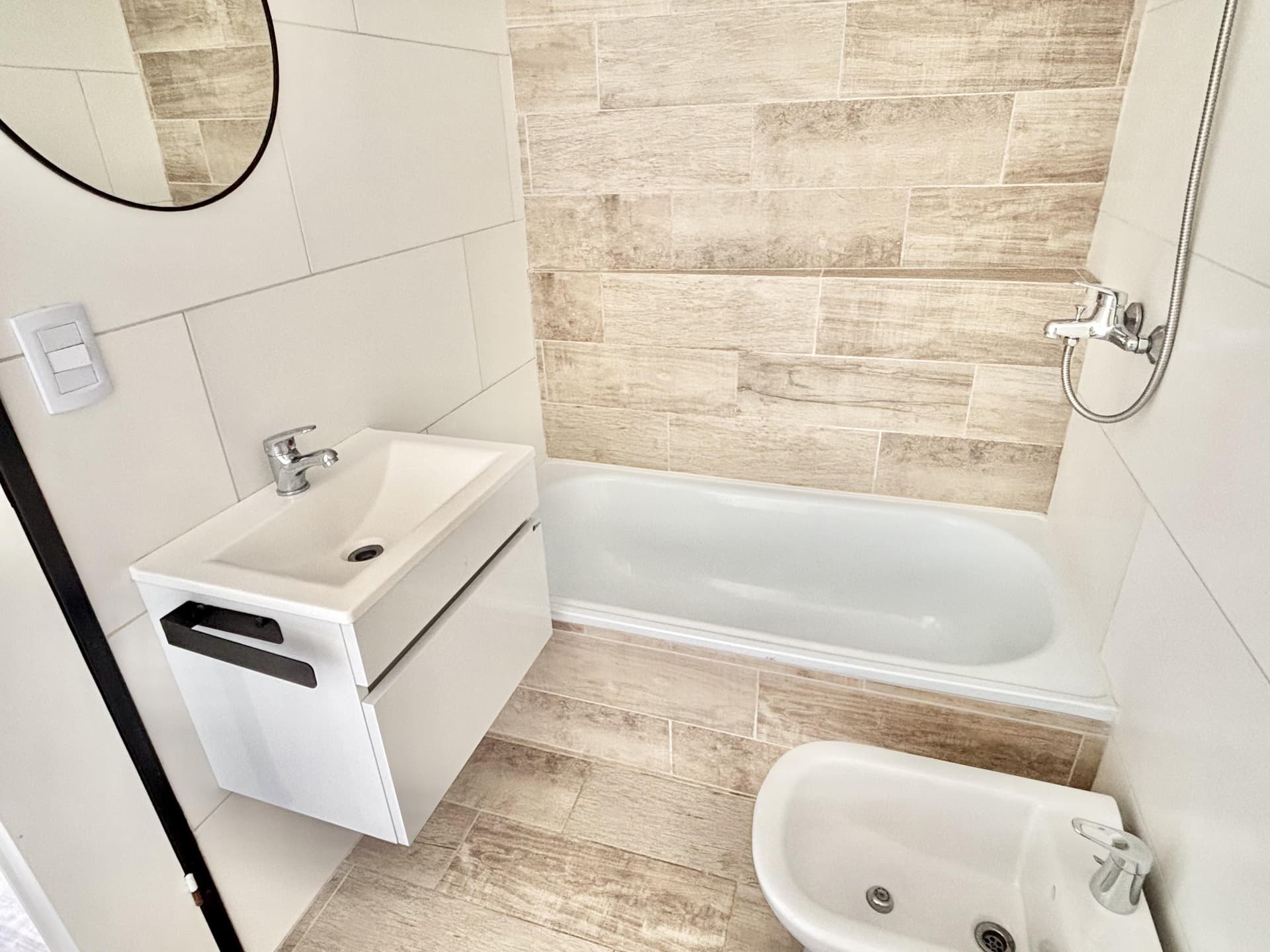 Baño con bañera, bidet, inodoro, vanitory y espejo redondo.