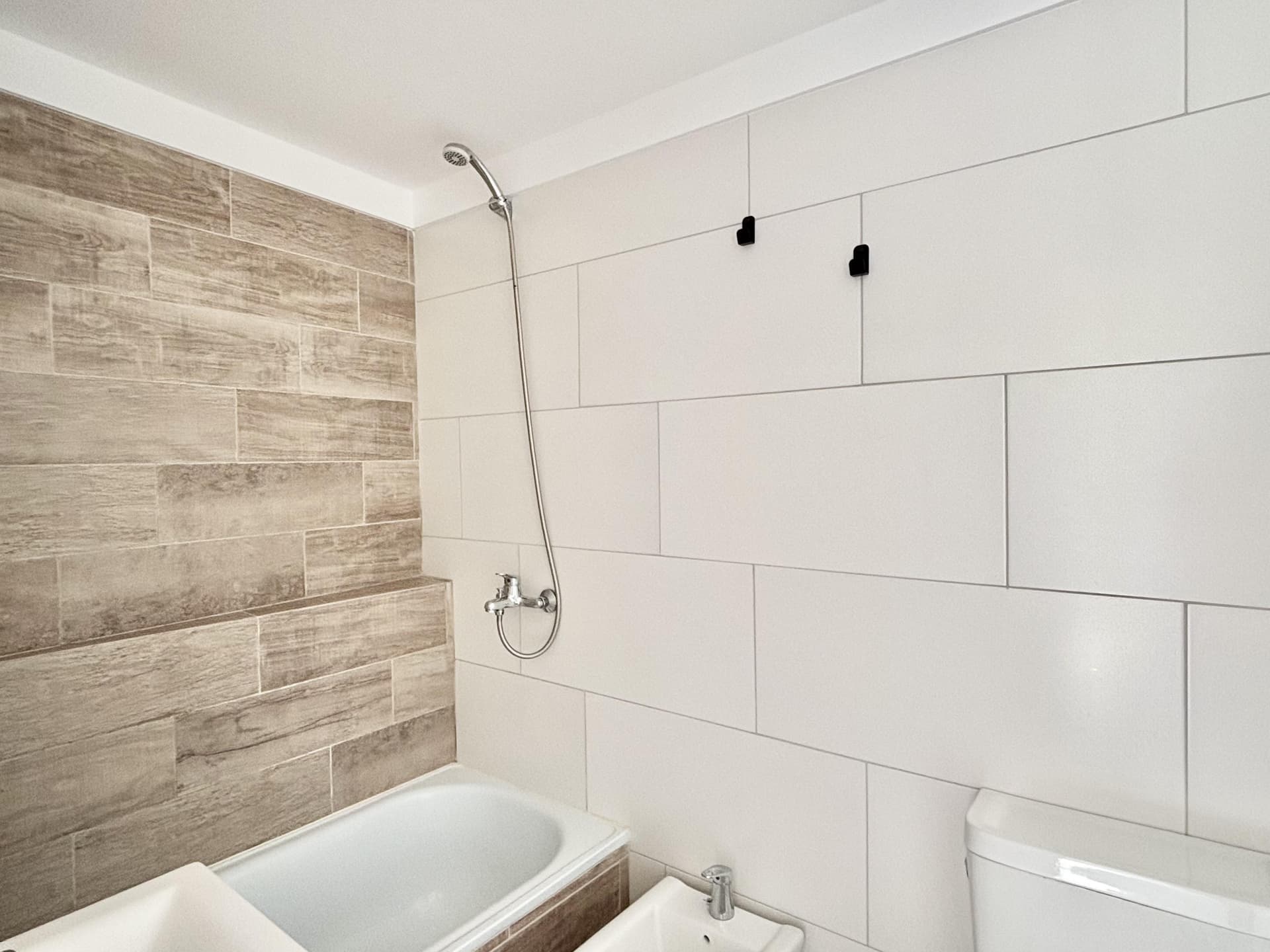 Baño con bañera, ducha y revestimientos cerámicos en tonos neutros.