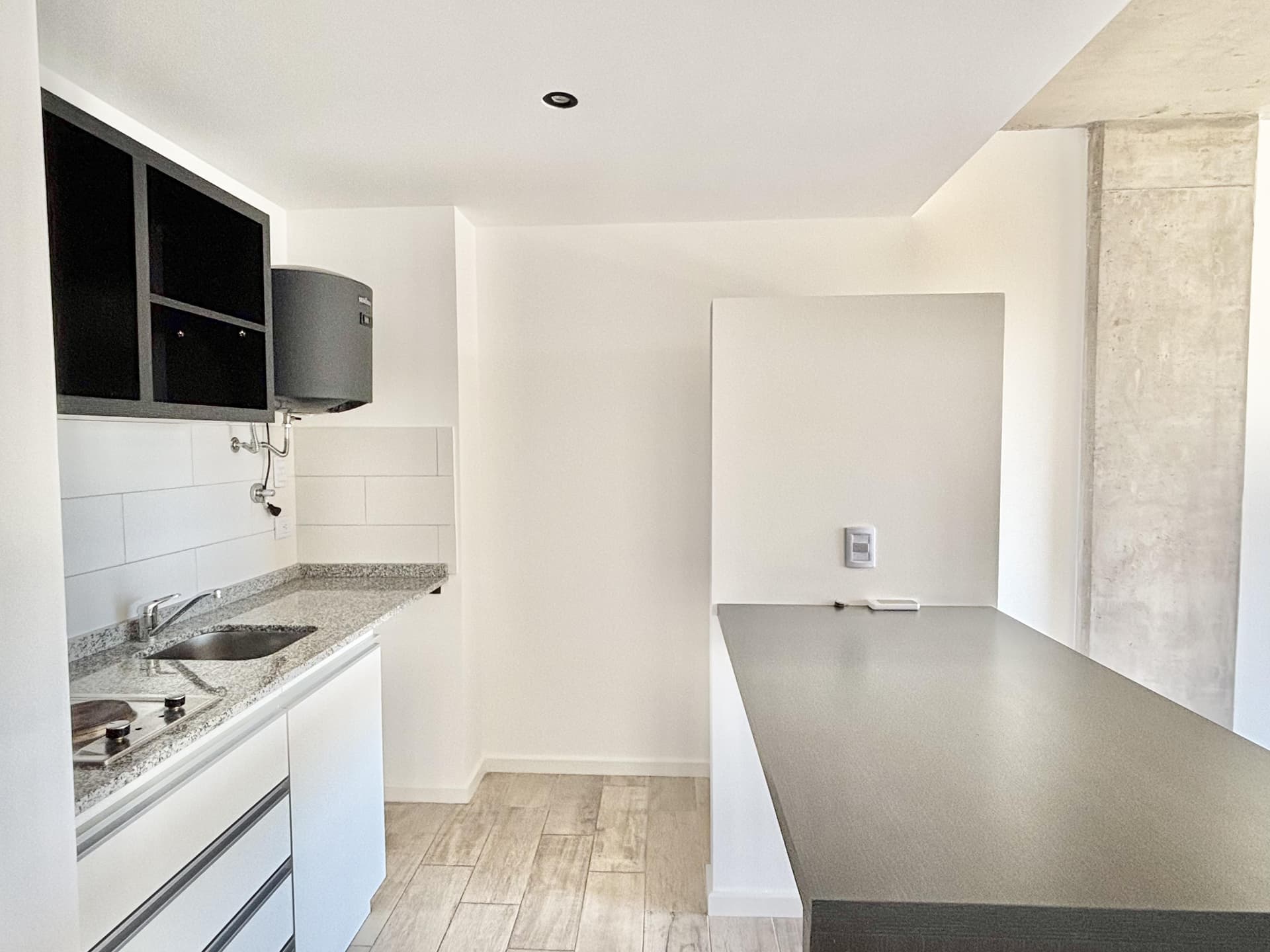 Cocina integrada con mesada gris, bacha y anafe eléctrico.