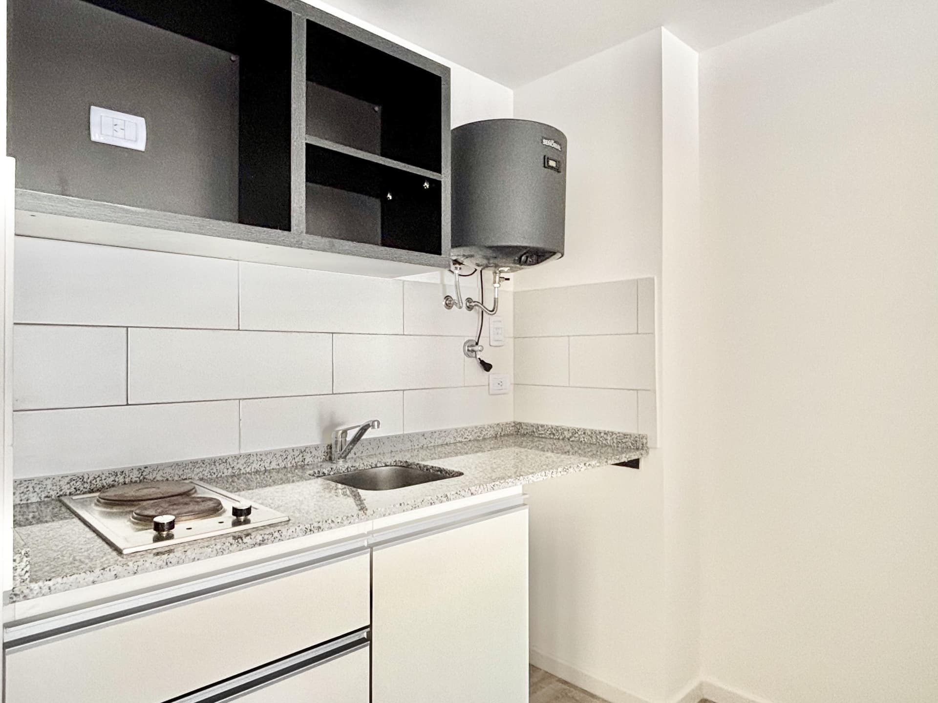 Detalle de cocina con mesada de granito, bacha, anafe y termotanque.