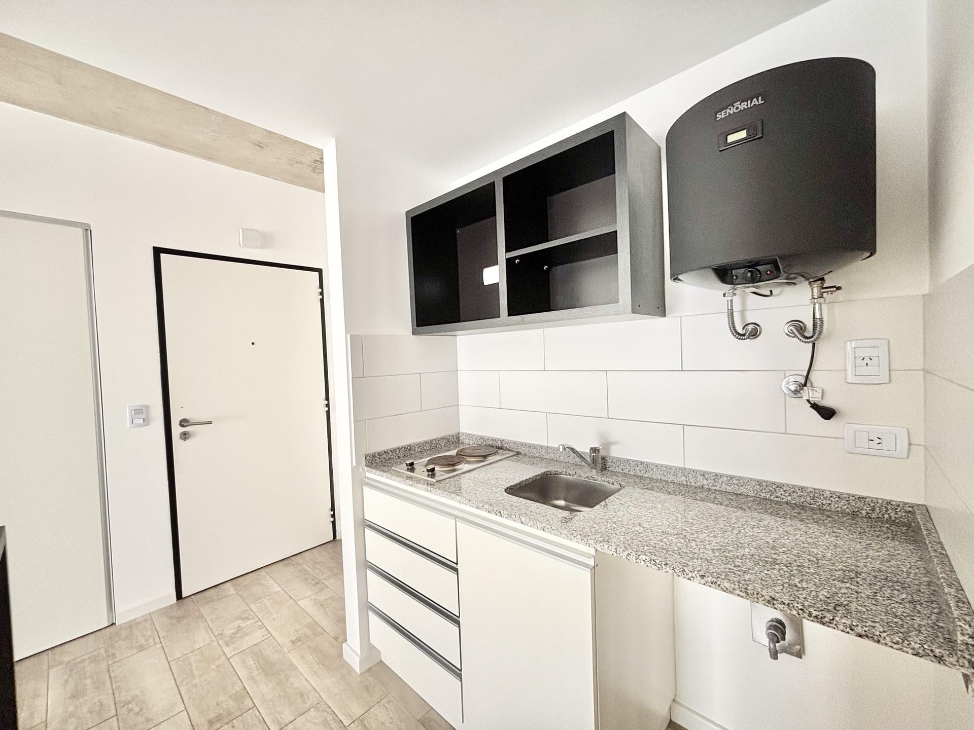 Cocina con bacha, anafe, termotanque y puerta de entrada en el fondo.