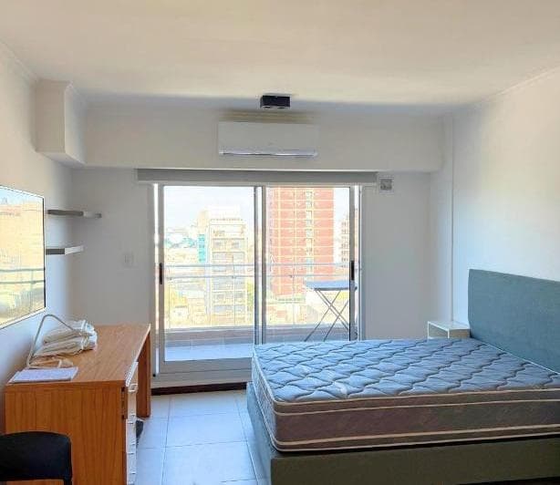 Living con cama, escritorio y acceso al balcón.