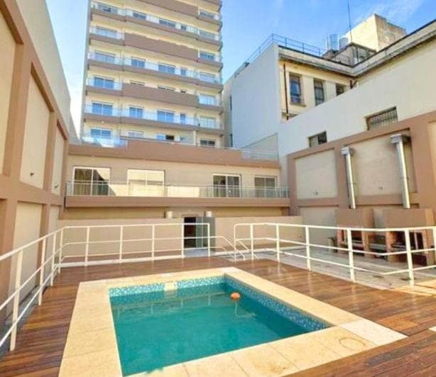 Pileta exterior comunitaria en deck de madera, con edificios.