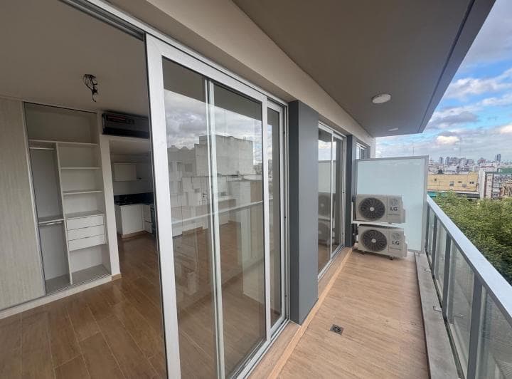 Balcón con piso de madera, baranda de vidrio y unidades de aire acondicionado.