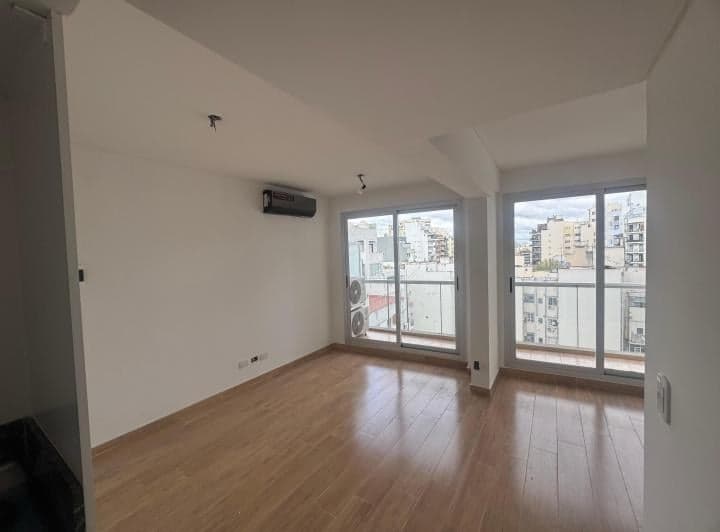 Living vacío con piso de madera y amplios ventanales al balcón.
