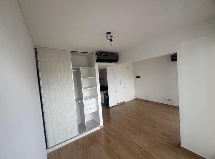 Living con placard integrado, cocina en el fondo y piso de madera.
