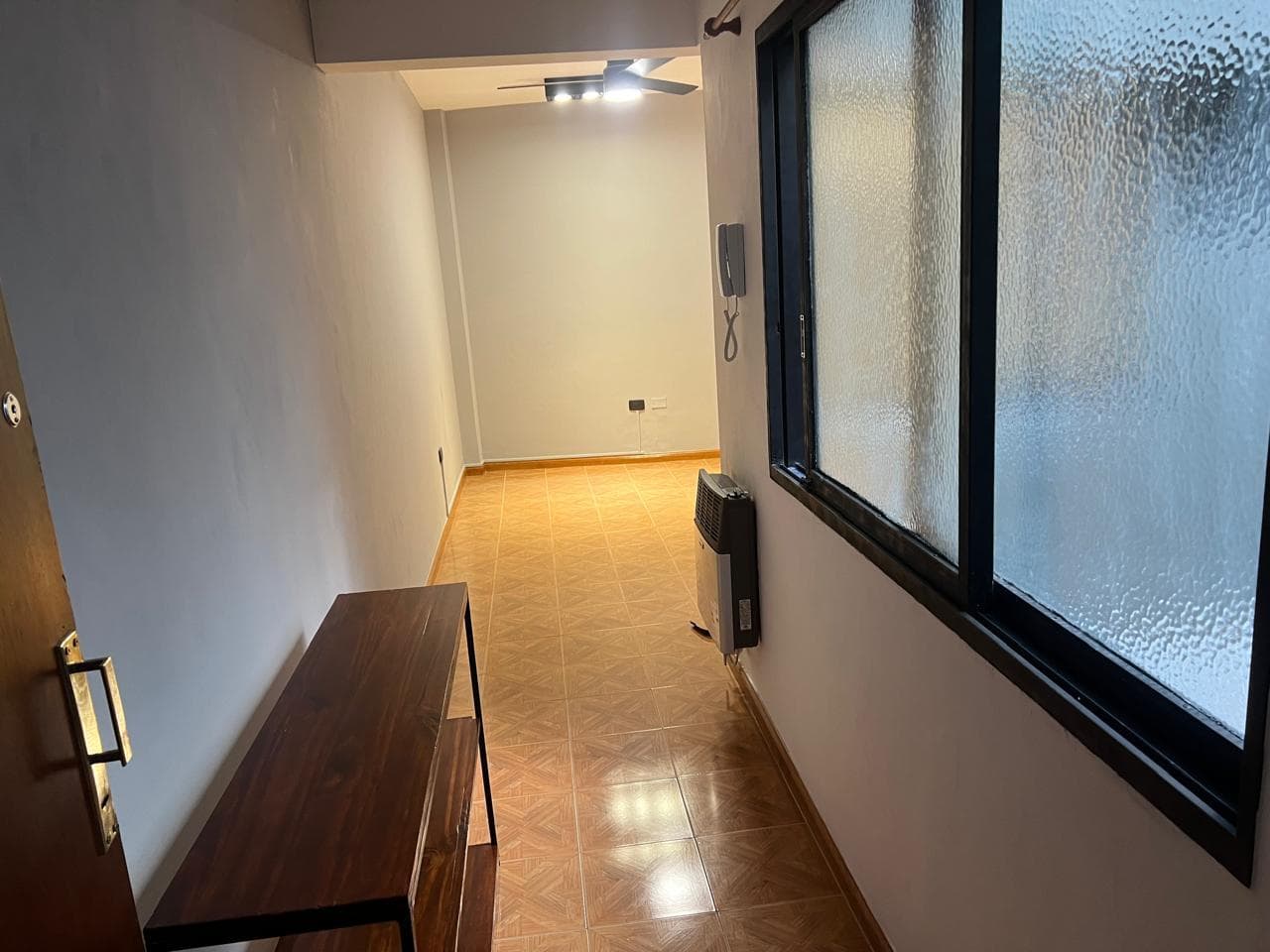 Living vacío con piso cerámico y estufa a gas, vista desde la entrada.