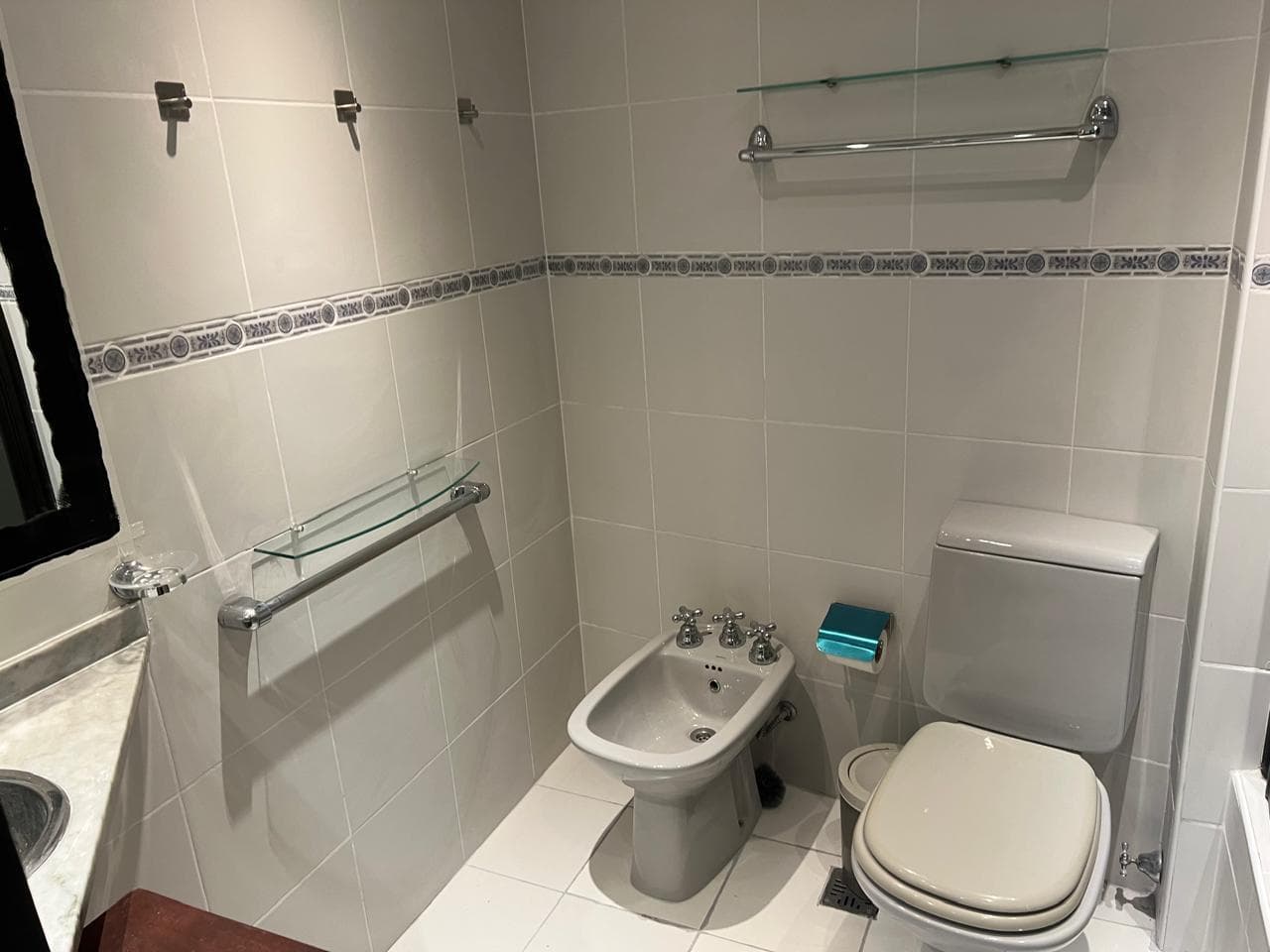 Baño con inodoro, bidet y vanitory con azulejos claros.