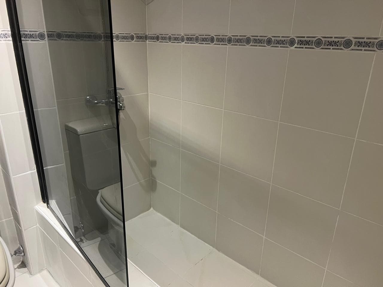 Mampara de vidrio en el baño, con azulejos claros.
