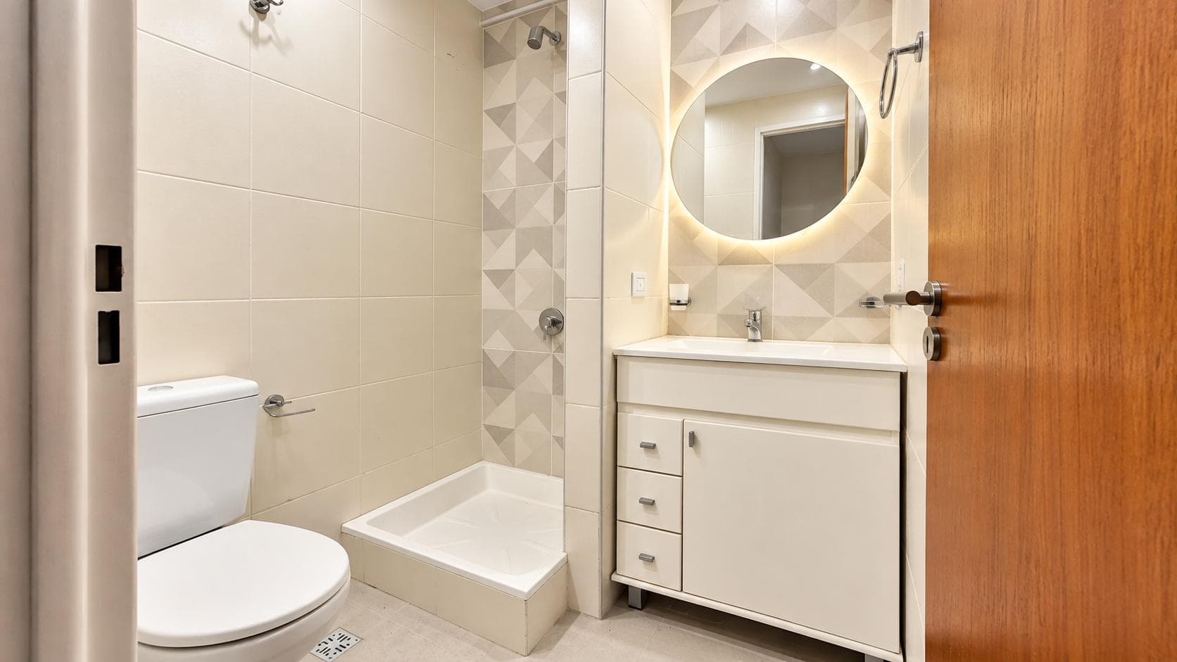 Baño con inodoro, vanitory y ducha, con revestimiento de azulejos geométricos.
