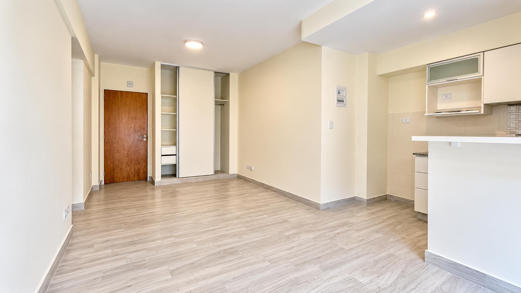 Ambiente abierto con placard blanco empotrado y piso de madera claro.