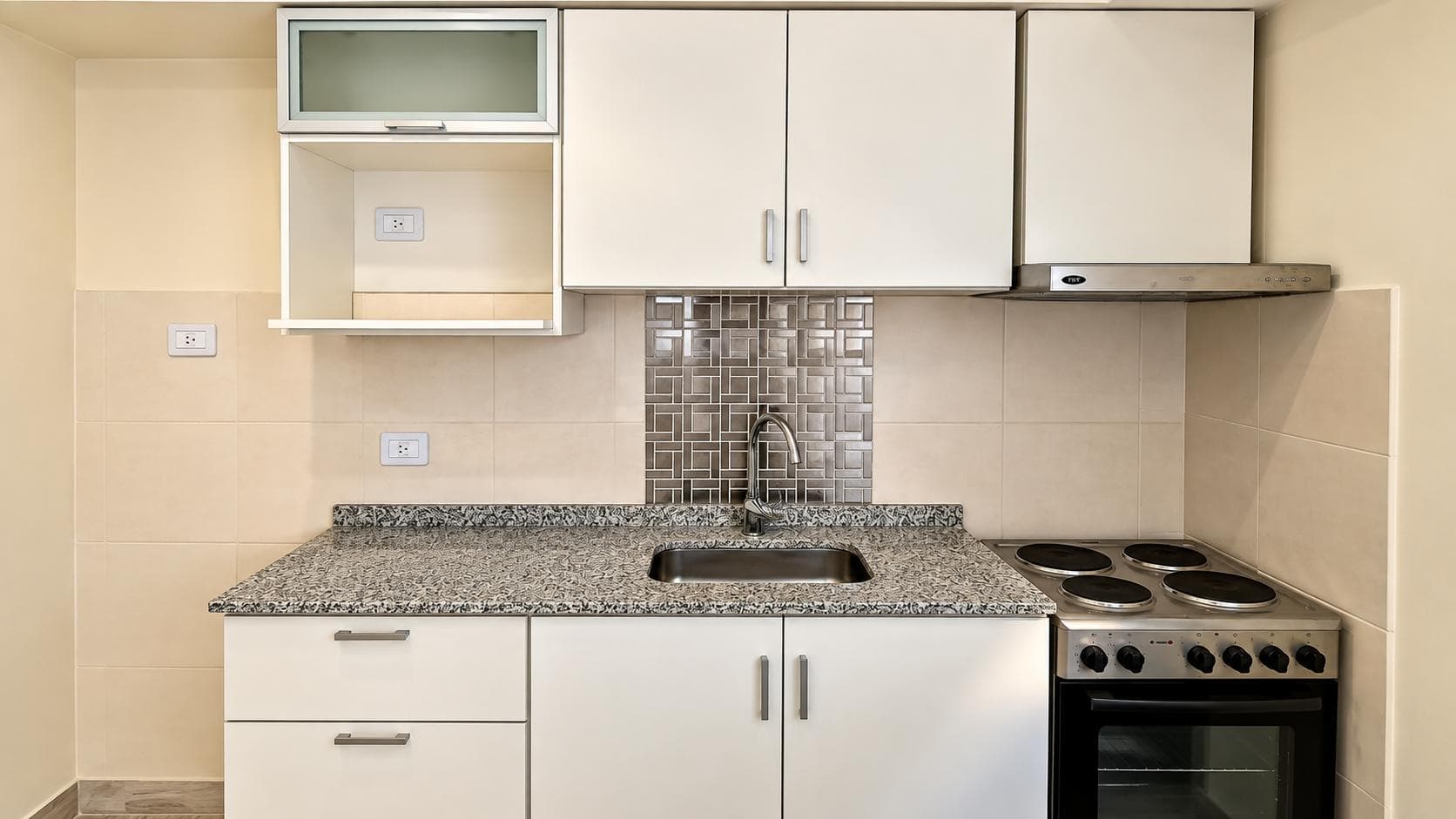 Detalle de cocina con bacha, anafe, horno, alacenas blancas y azulejos brillantes.