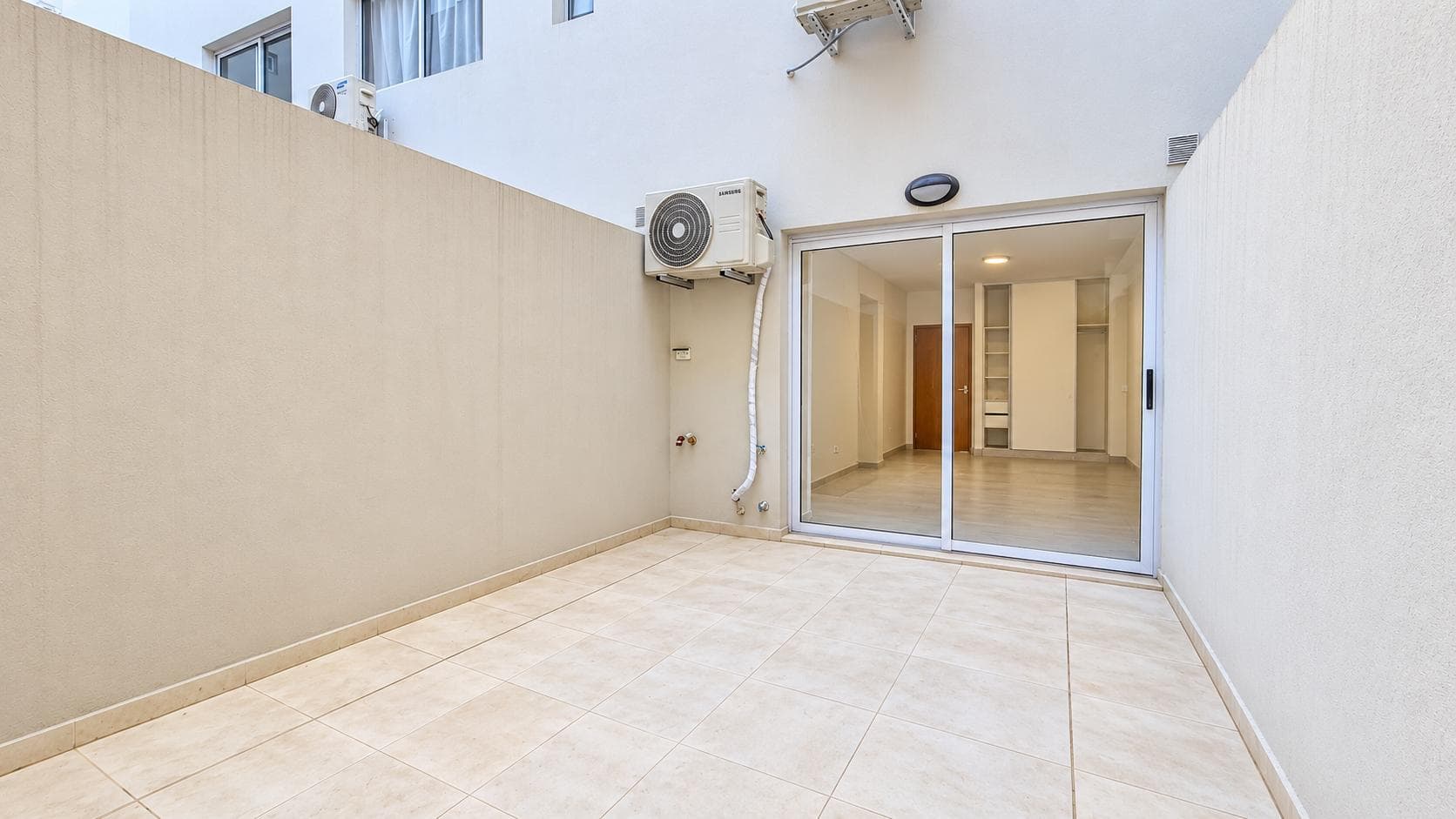 Patio con piso de baldosas, unidades de aire acondicionado y salida al interior.