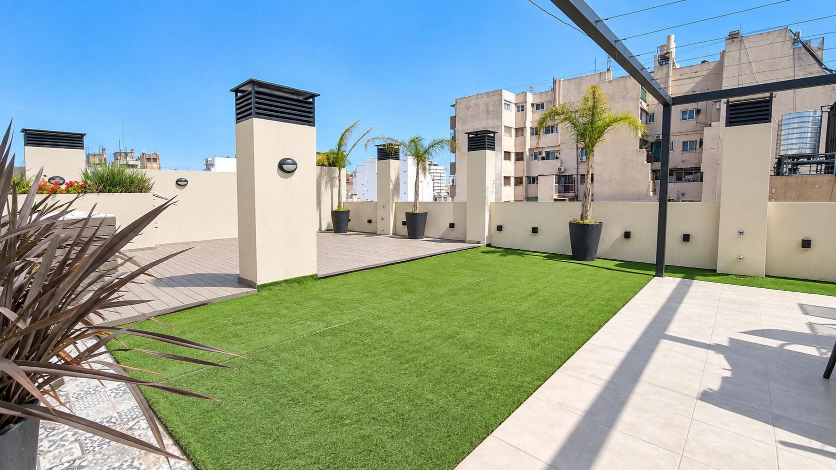 Terraza común con césped sintético, macetas decorativas y vista a edificios.