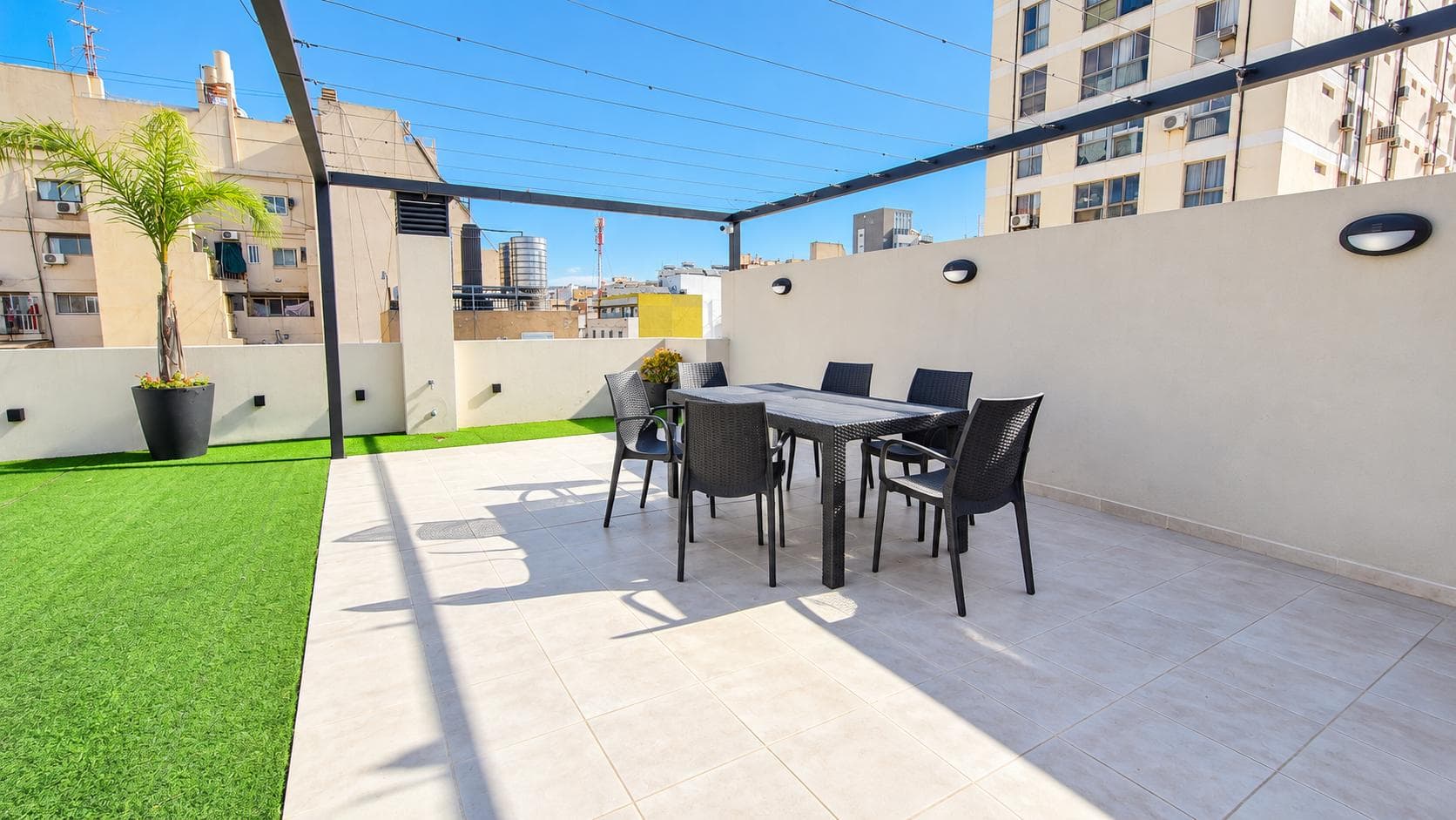 Terraza con mesa y sillas de exterior bajo pérgola, césped sintético.