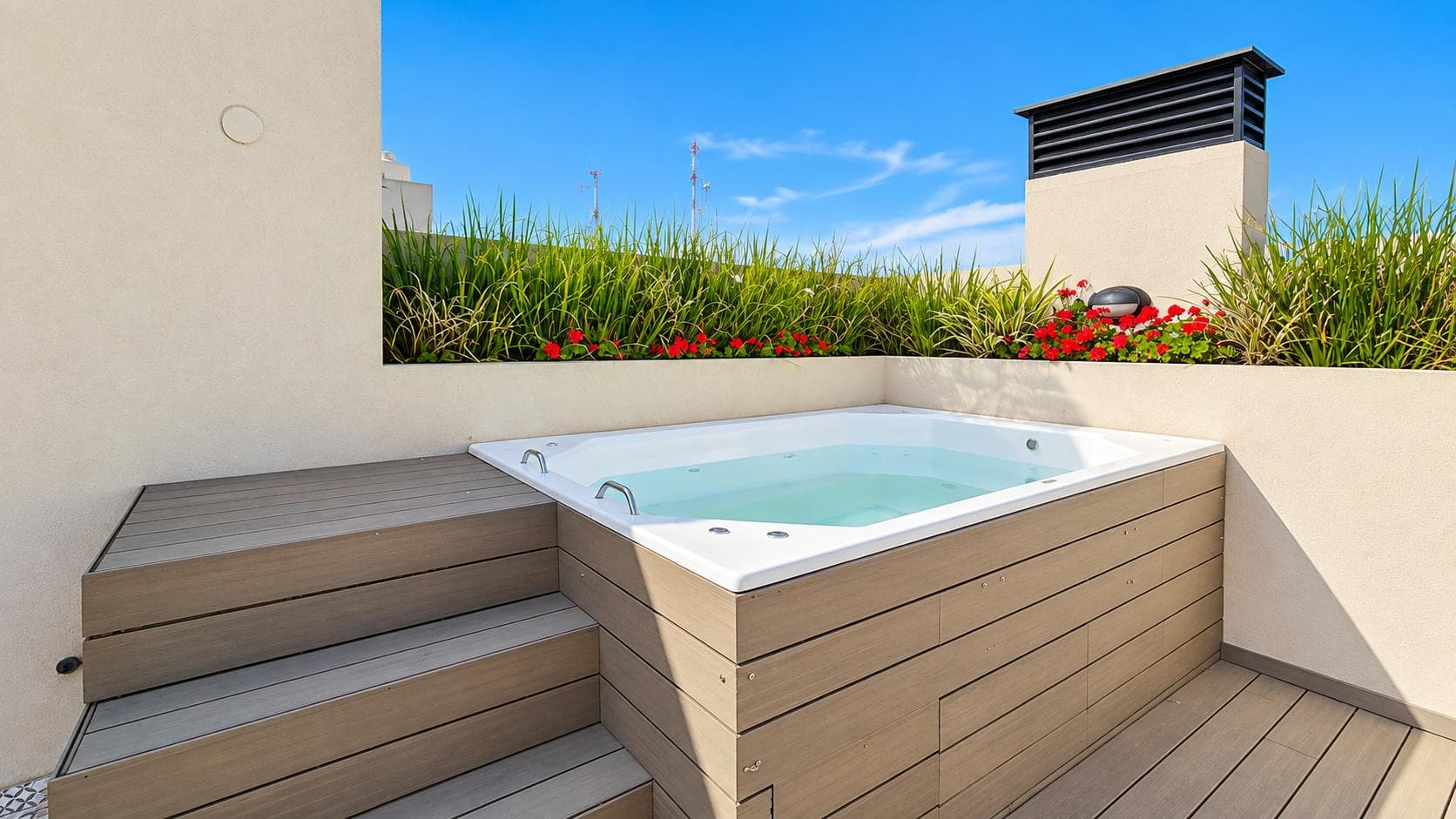 Detalle de jacuzzi en terraza con deck de madera y plantas con flores rojas.