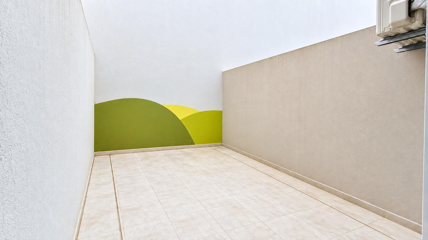 Patio con pared decorada con formas verdes y amarillas y piso cerámico.