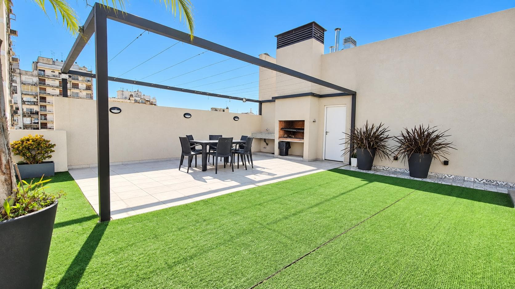 Terraza con pasto sintético, parrilla, mesa con sillas y sol pleno.