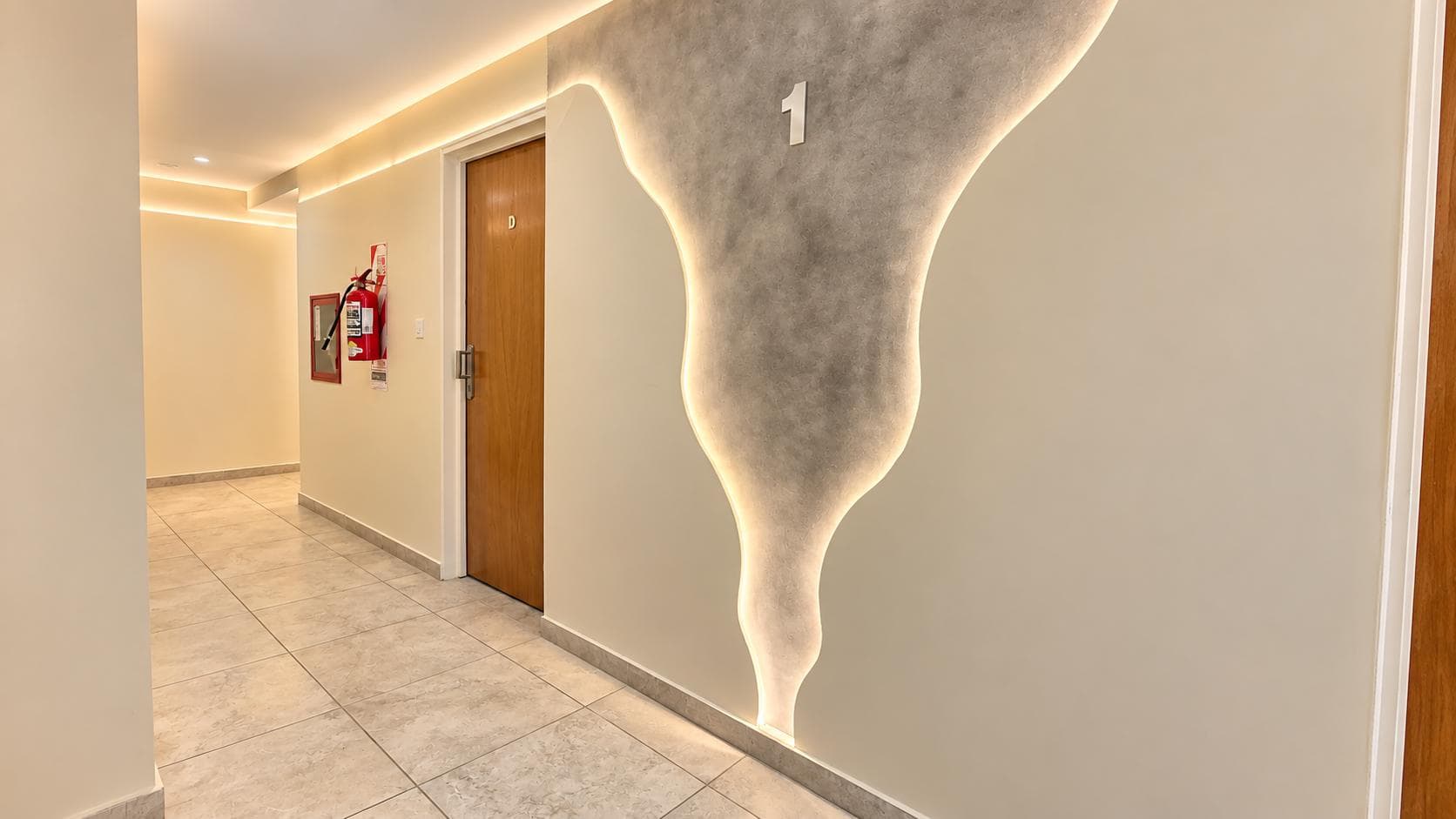 Pasillo de edificio con diseño iluminado en pared y puerta de madera.